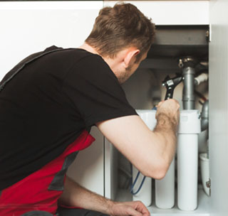 Le plombier de la cuisine installe un système de traitement de l'eau domestique. Système de flasque à trois étages